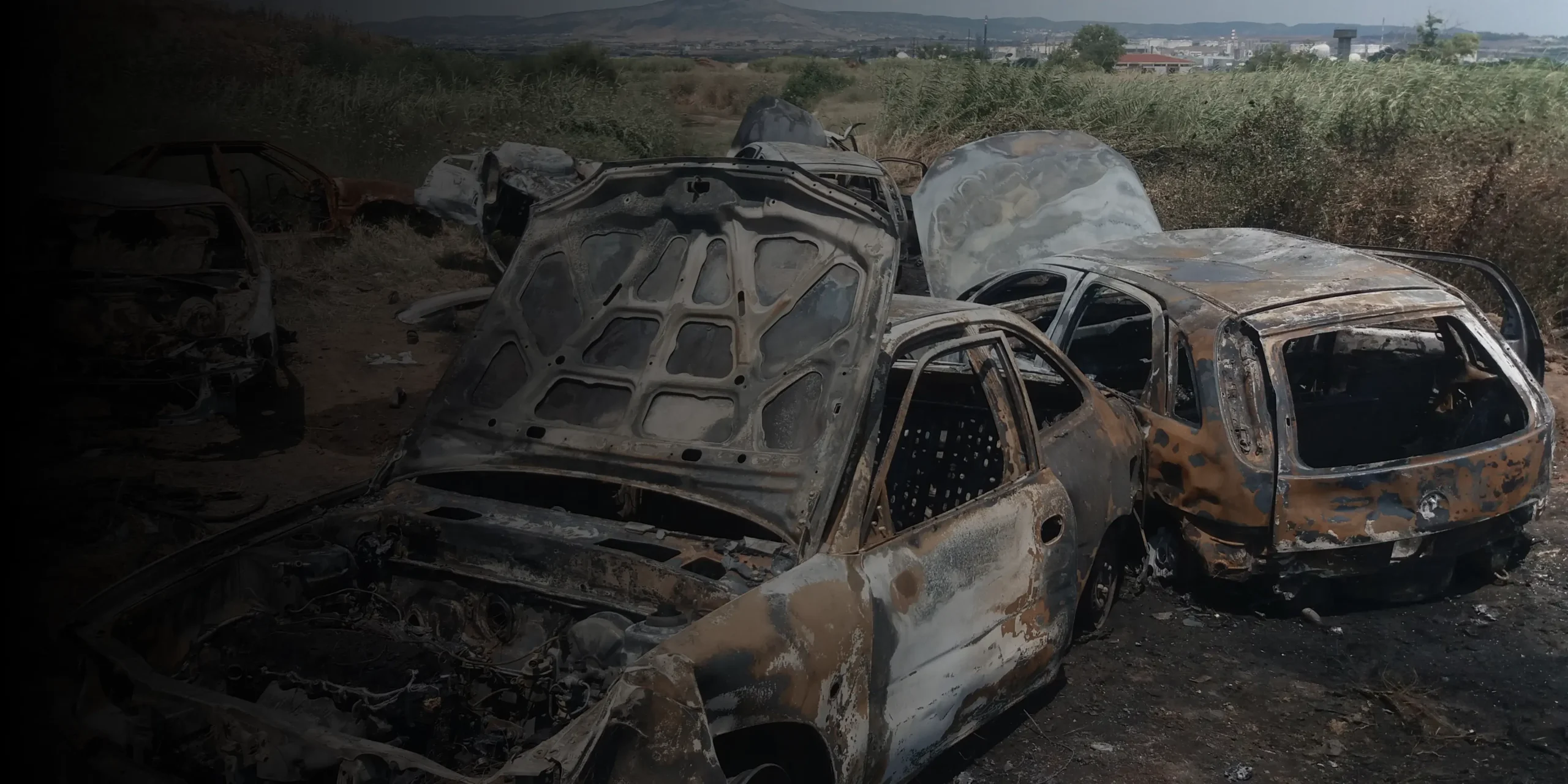 Burned and rusted cars in a scrapyard or field
