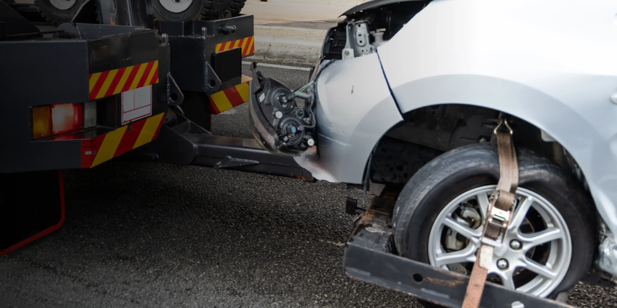 Tow truck hauling a damaged silver car