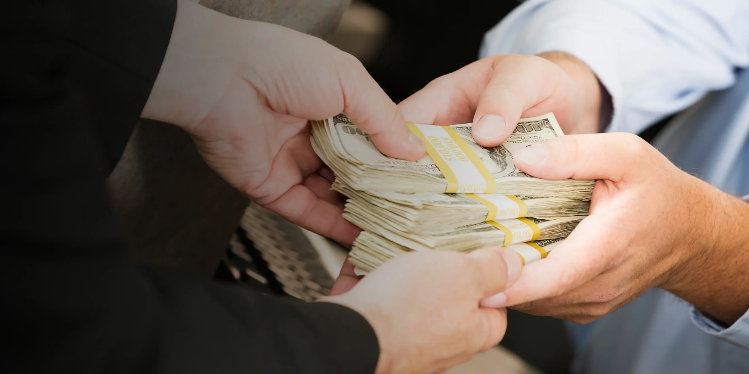Close-up of hands exchanging stacks of U.S. dollars